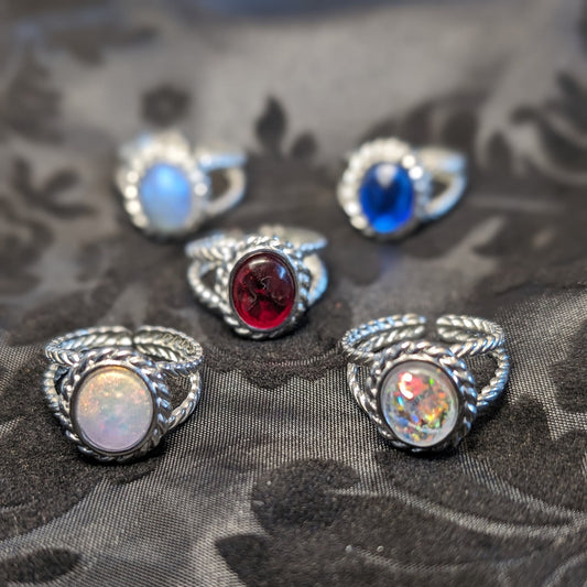 Five rings with resin cabochons and braided stainless steel bezels sit on a black fabric background